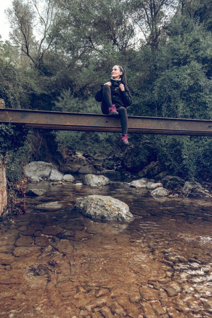 Cheerful traveler sitting on bridge over calm river in amazing park